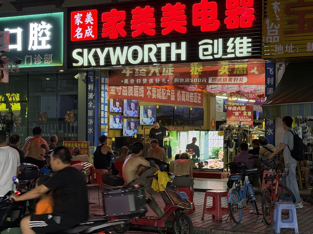 路过一家电器店,店前人们围着一台大彩电坐在外面看电影,路过的行人也时常驻足,这个画面是这台电视的最好的广告。